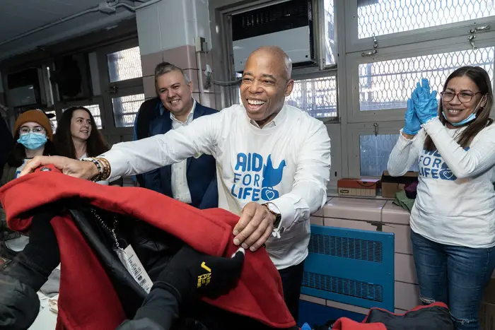 Mayor Eric Adams hands someone a red coat during a food and clothing distribution event.